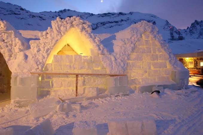 Ice-block walls of a small building beside a frozen mountain lake